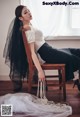 A woman sitting on a wooden chair with a veil over her head.