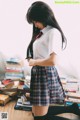 A woman in a school uniform standing in front of a pile of books.