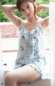 A woman sitting on a window sill wearing a blue floral dress.