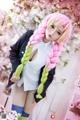A woman with long pink and green hair standing in front of flowers.